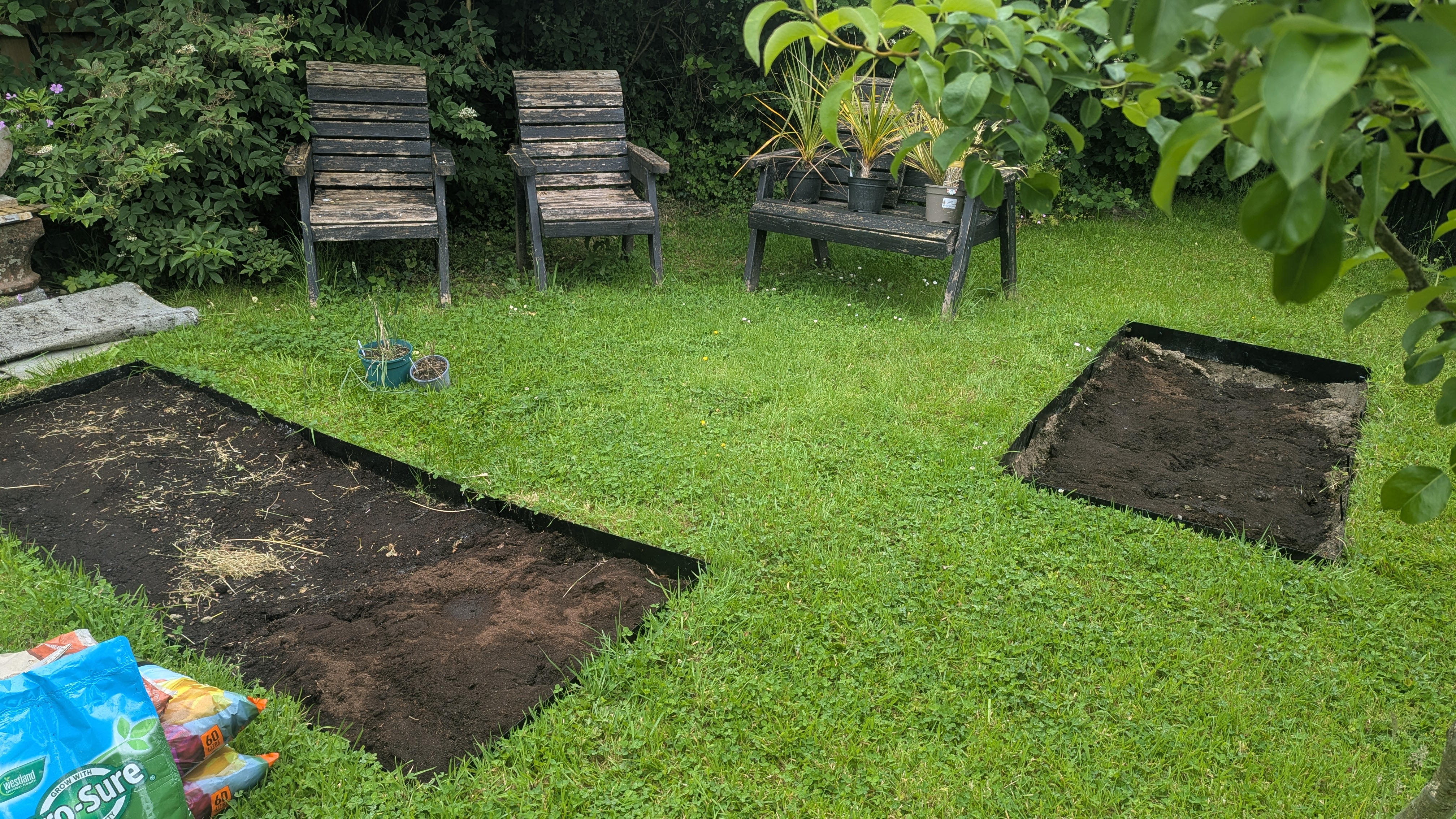 Two freshly dug rectangular planting beds cut into a lawn in Llanfallteg near Whitland, with lawn edging strip fitted and bags of compost on standby
